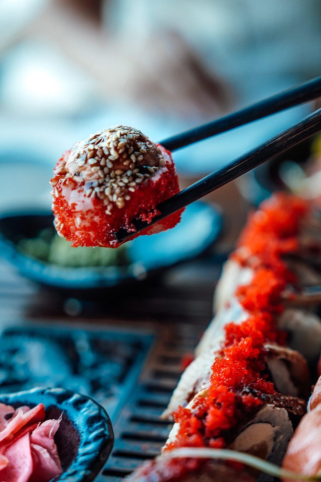 Roll with tobiko and sesame held with chopsticks
